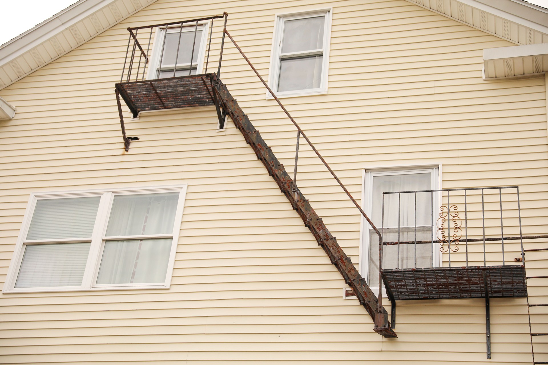 view of fire escapes on buildings and houses. A series of metal ladders and platforms are visible on the exterior walls of the structures. Captures the urban aesthetic of the fire escape.