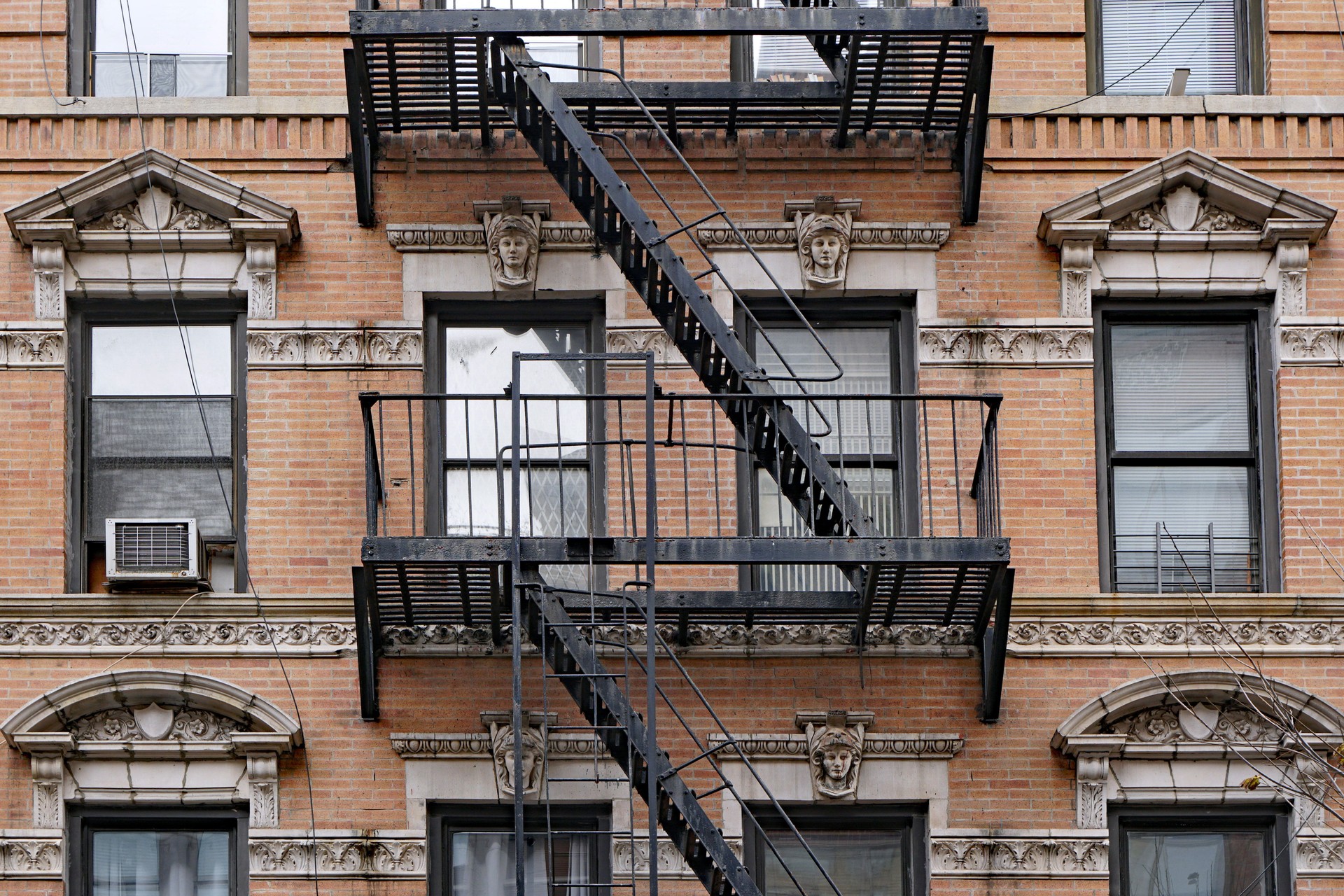 Old fashioned Manhattan apartment building facade with ornate decorative stone carving and external fire escape ladders