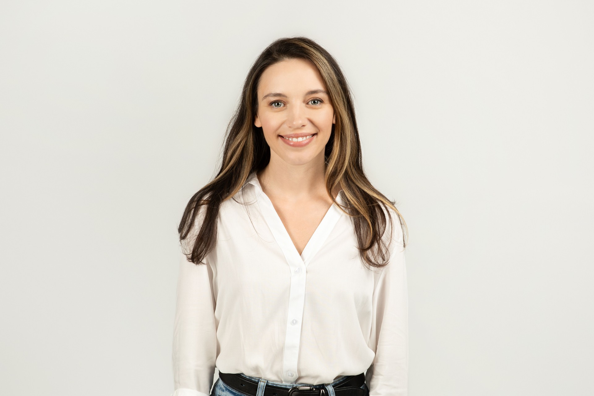 A friendly young woman with long brunette hair, wearing a crisp white blouse and blue jeans