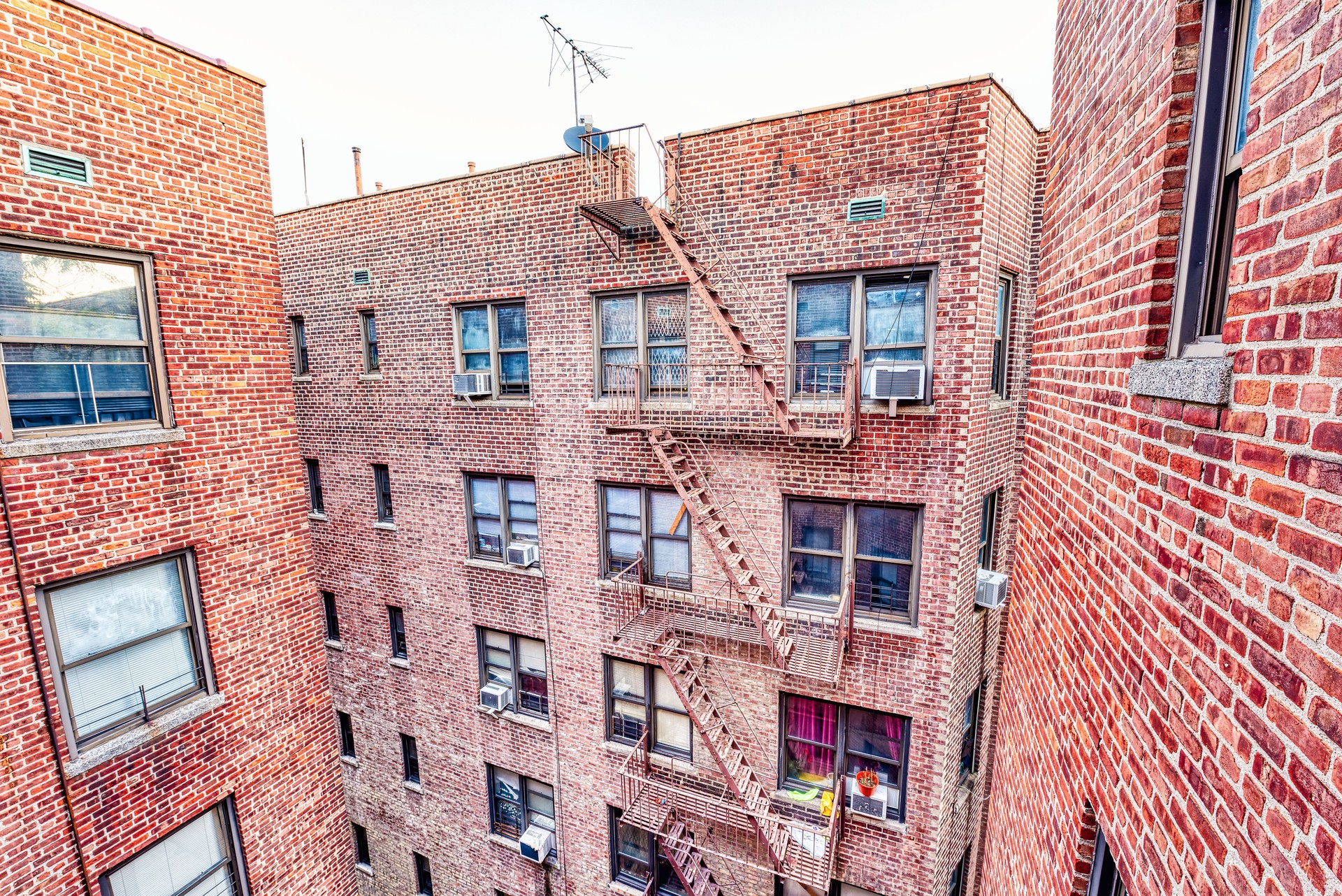 Brick apartment condo building roof exterior architecture in Fordham Heights center, Bronx, NYC, Manhattan, New York City with fire escapes, windows, ac units in morning, satellite dish, antenna