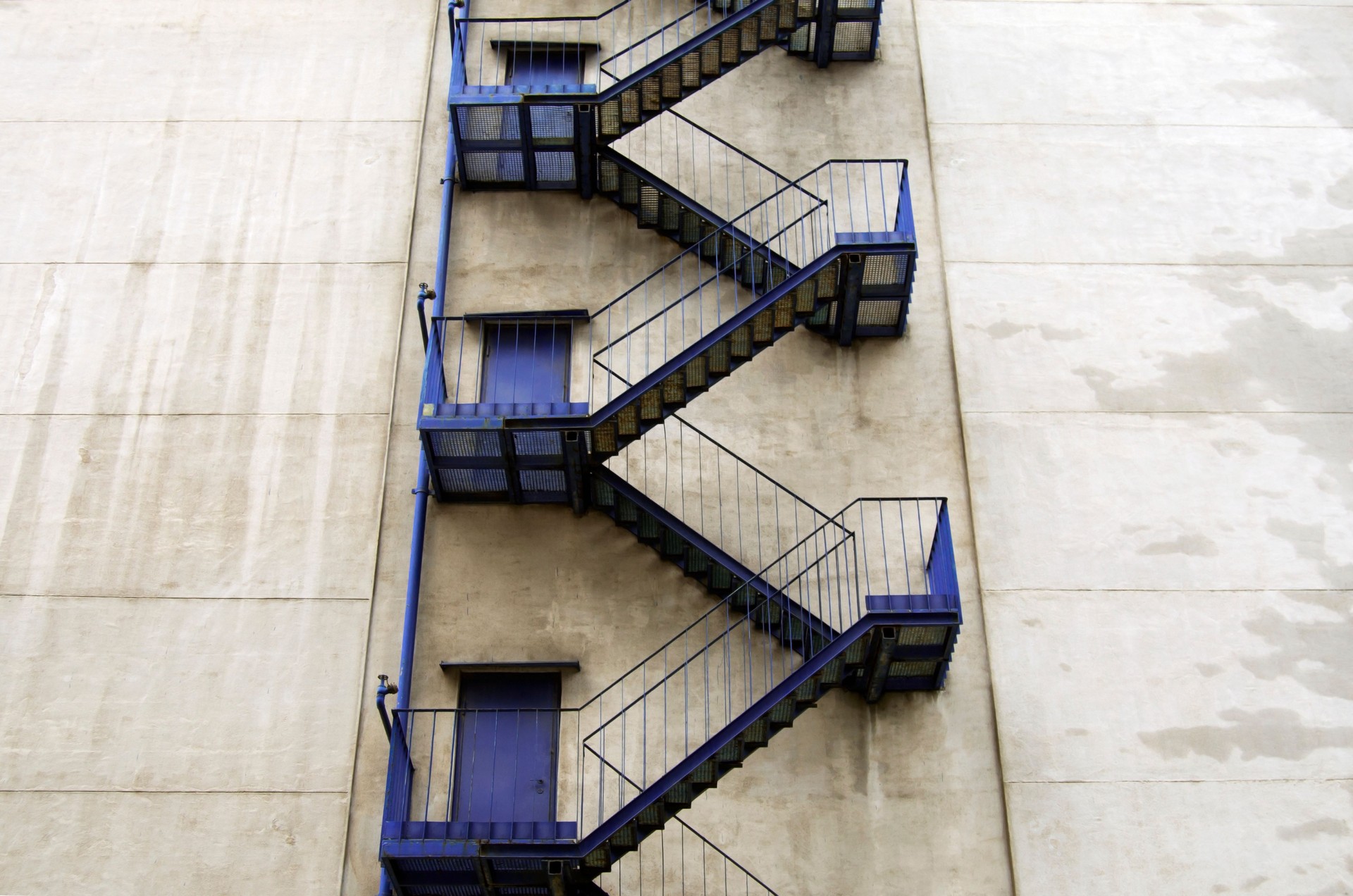 Exterior blue fire escape staircase in high-rise grey building.