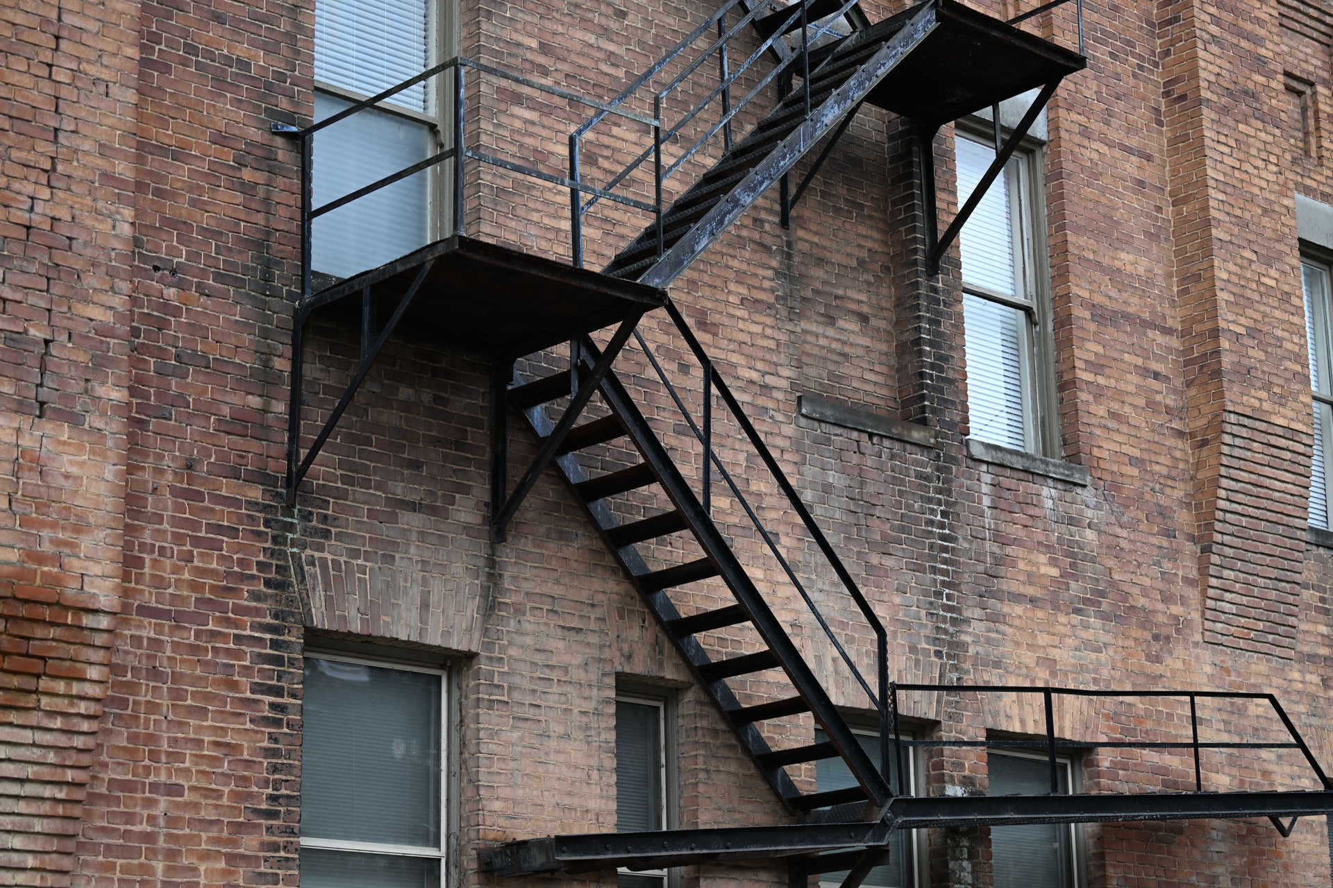 Exterior black fire escape staircase attached to the side of a red brick building